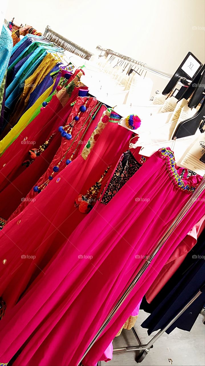 Vibrant colored skirts from India getting ready to be used for a performance. Hanging on a garment rack with tags.