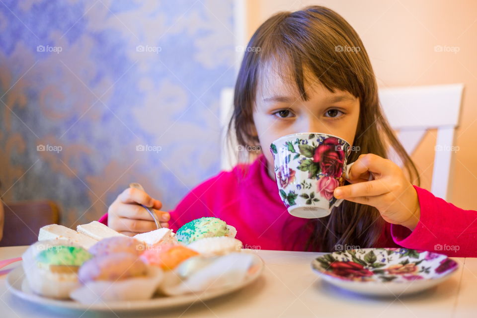 Little girl with cup of tea and cupcakes 