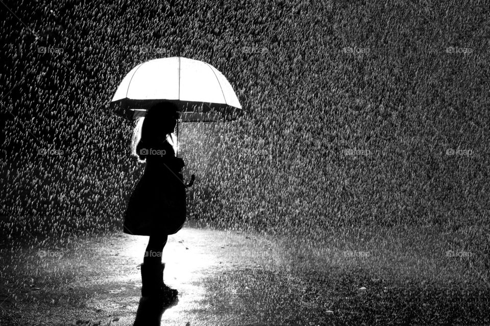 Silhouette of little girl and see through umbrella standing in the rain. Black and white image