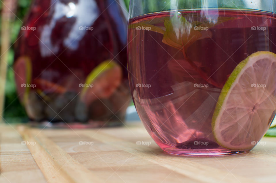 Low angle view of fresh homemade flavored water with mint, lime and blueberry on wood table next to large pitcher conceptual healthy lifestyle, hydration and beautiful summer drink photography