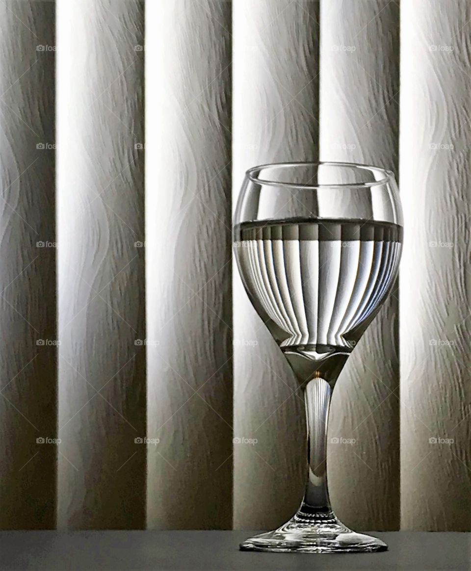 Wine glass with water in it reflecting the window blinds