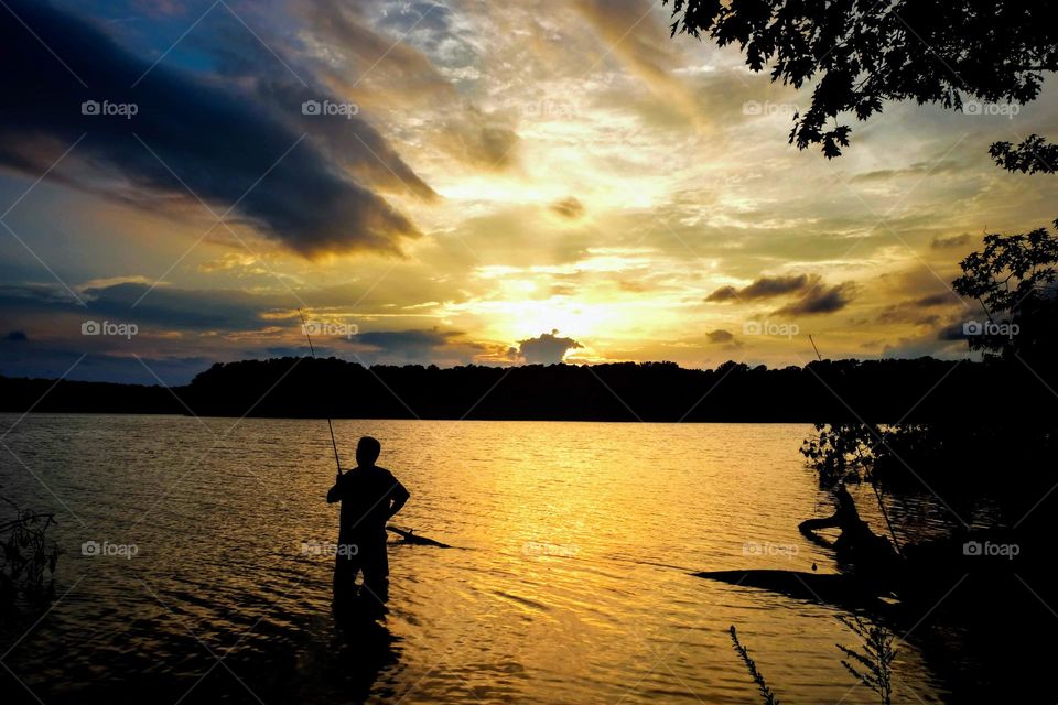 Clouds filter the setting sunlight for the fisherman. Lake Benson, Garner, North Carolina. 