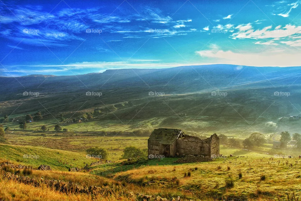 A deep valley cuts through green countryside with a deserted barn on its slopes.