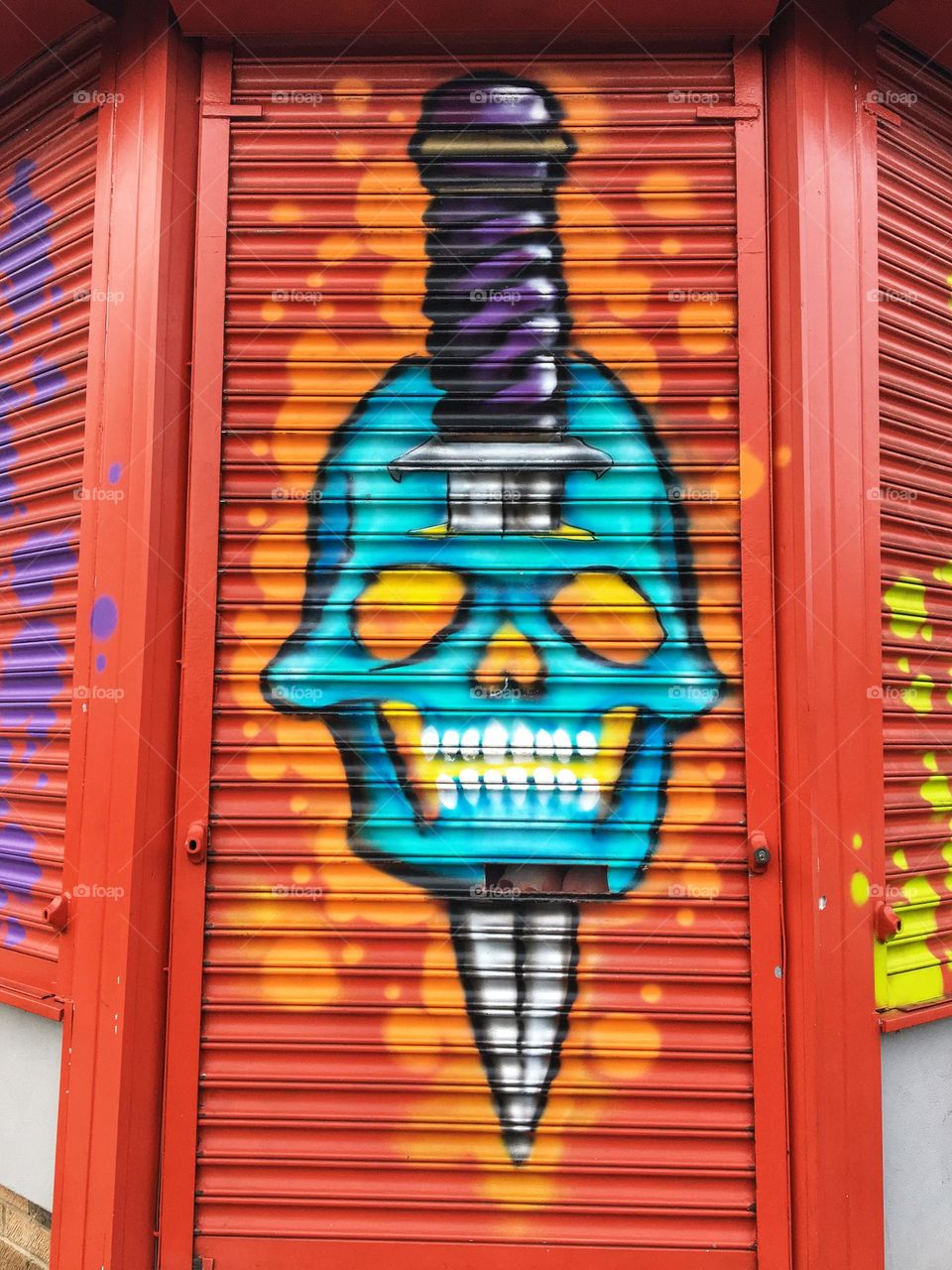 Rather gory skeleton with a dagger through its head that is painted onto door shutters of a tattoo parlour 