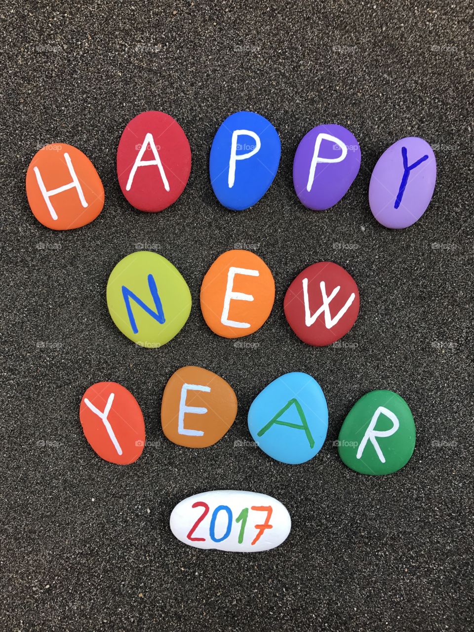 Happy New Year 2017 on multicolored stones over volcanic black sand