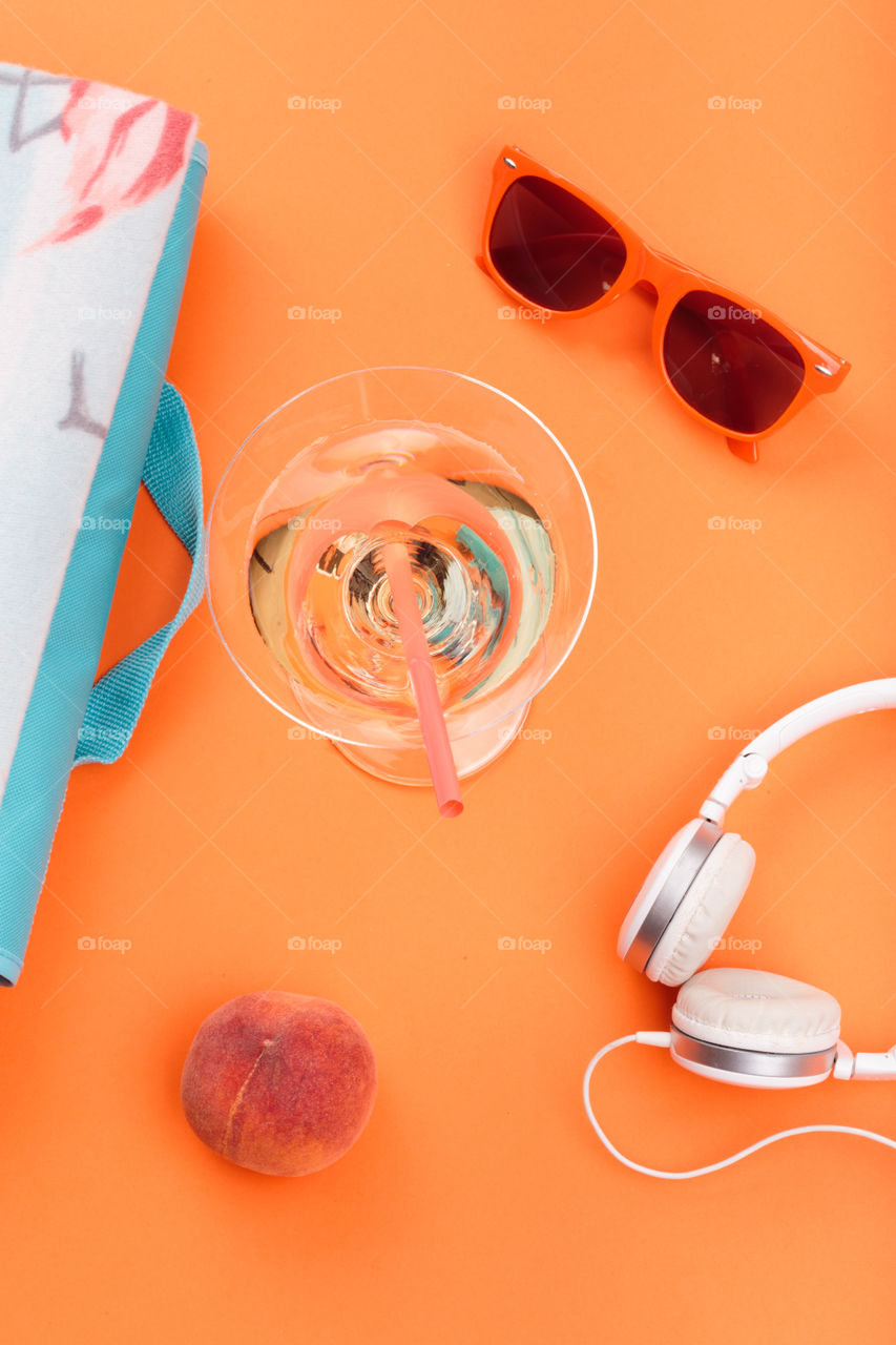 Sunglasses, glass with drink, headphones, peach, blanket on orange background. Minimal summer style