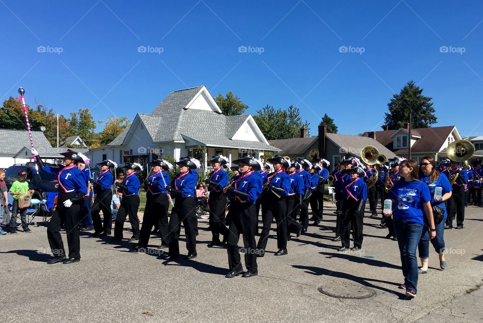 Marching band wearing blue jackets in small town parade. 