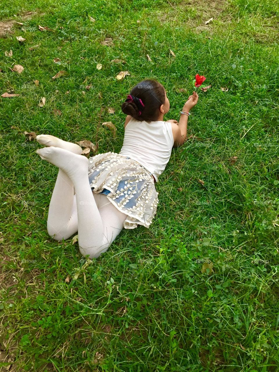 A little girl sleeping on the grass and holding a red flower