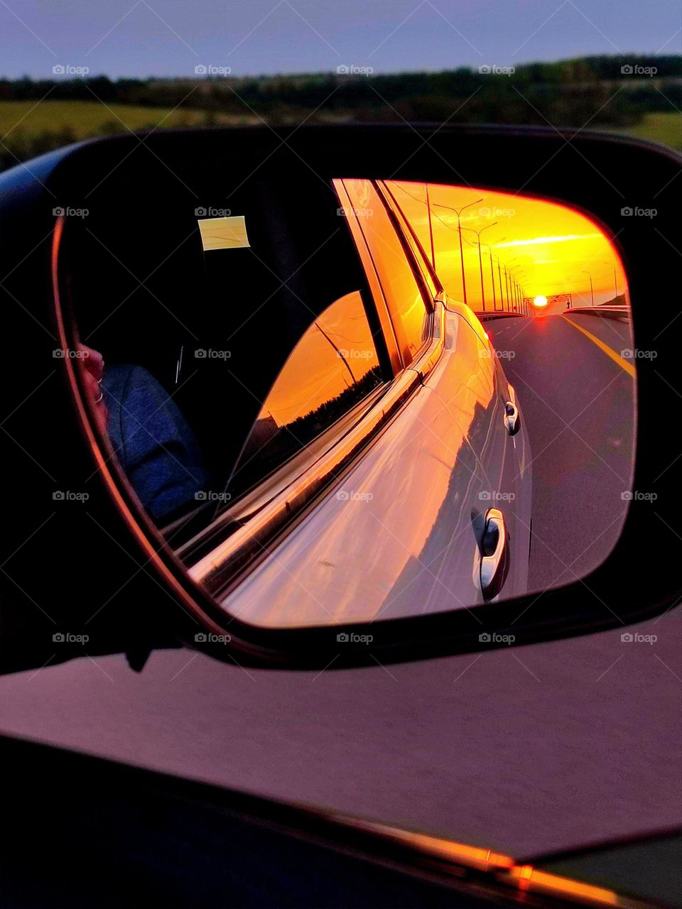 Travel by car.  The road is reflected in the side mirror of the car, the sunset is on the horizon.  The ability to get to any place: mountains, fields, sea. Anticipation of new adventures