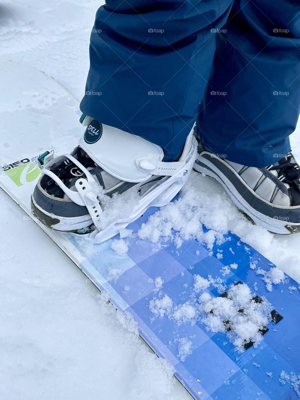 A snowboarder gets prepped by clipping their boots into a colorful board in the snow