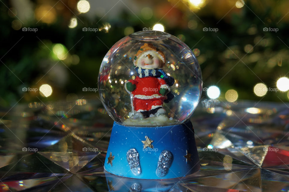 Christmas snow globe ball. Decorating Christmas dome ball before a lit Christmas tree.
