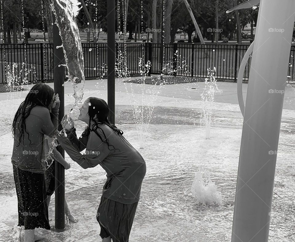 Children having fun in the city splash pad great memories full of silly and great moments with surprises and water pouring, splashing and spraying in black and white.