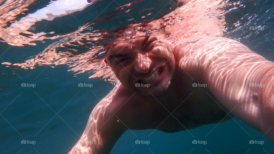 Man diving, man underwater smiling and relaxing in big blue sea