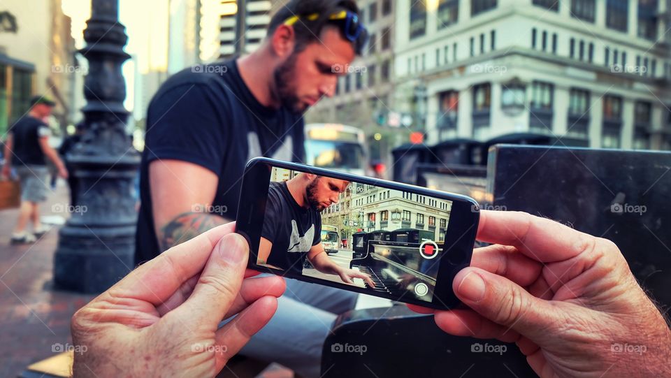 Human hand holding a mobile phone and taking video of pianist