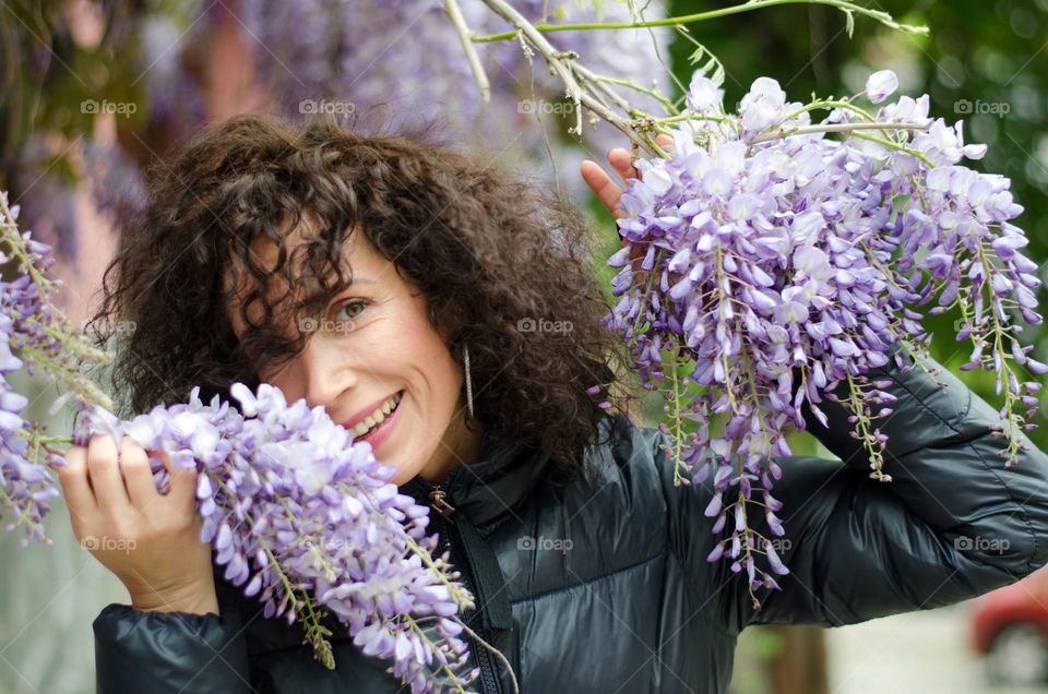 Portrait of a woman brunette with beautiful natural hair on background of purple flowers