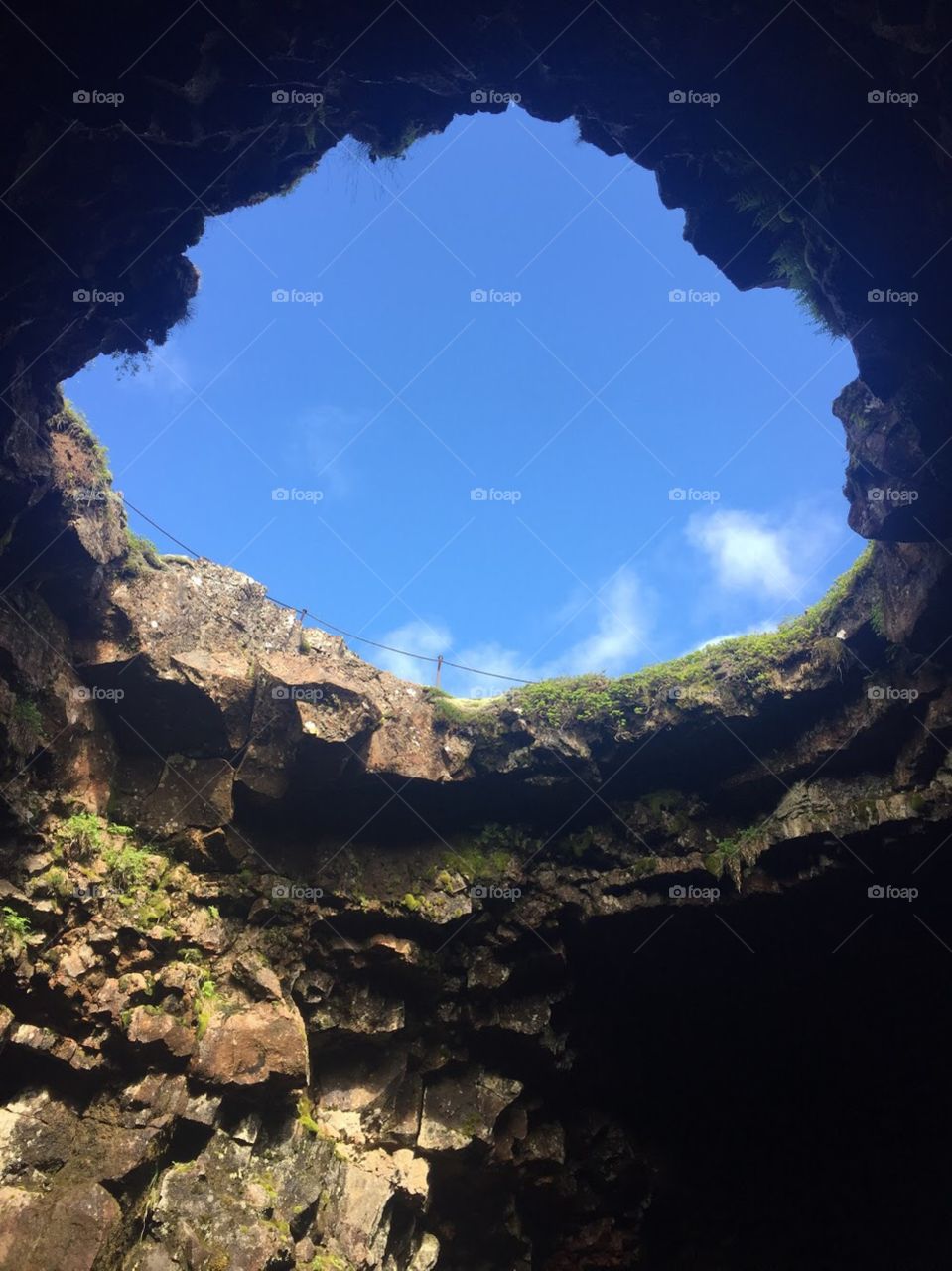 Hole in the roof of a cave, blue sky outside of the moss covered walls of the cave. 