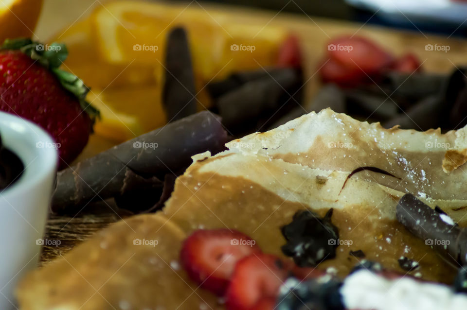 Fresh crepes with chocolate, fresh strawberry and blueberry on wood table in kitchen closeup conceptual cooking gourmet food photography background 