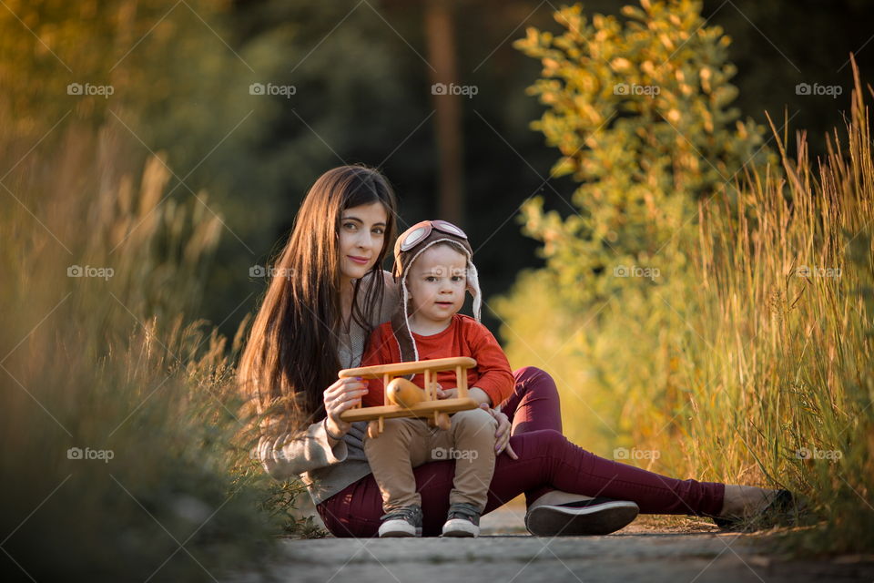 Mother with son playing with wooden plane at sunset