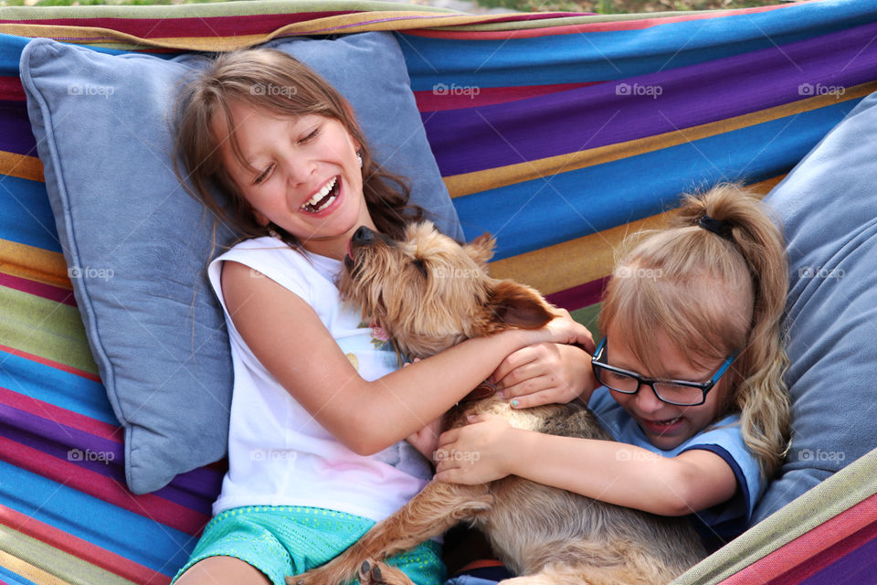 Sisters cuddling with dog in hammock