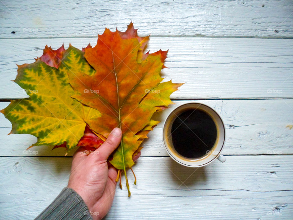 Person's hand with autumn leaves and coffee