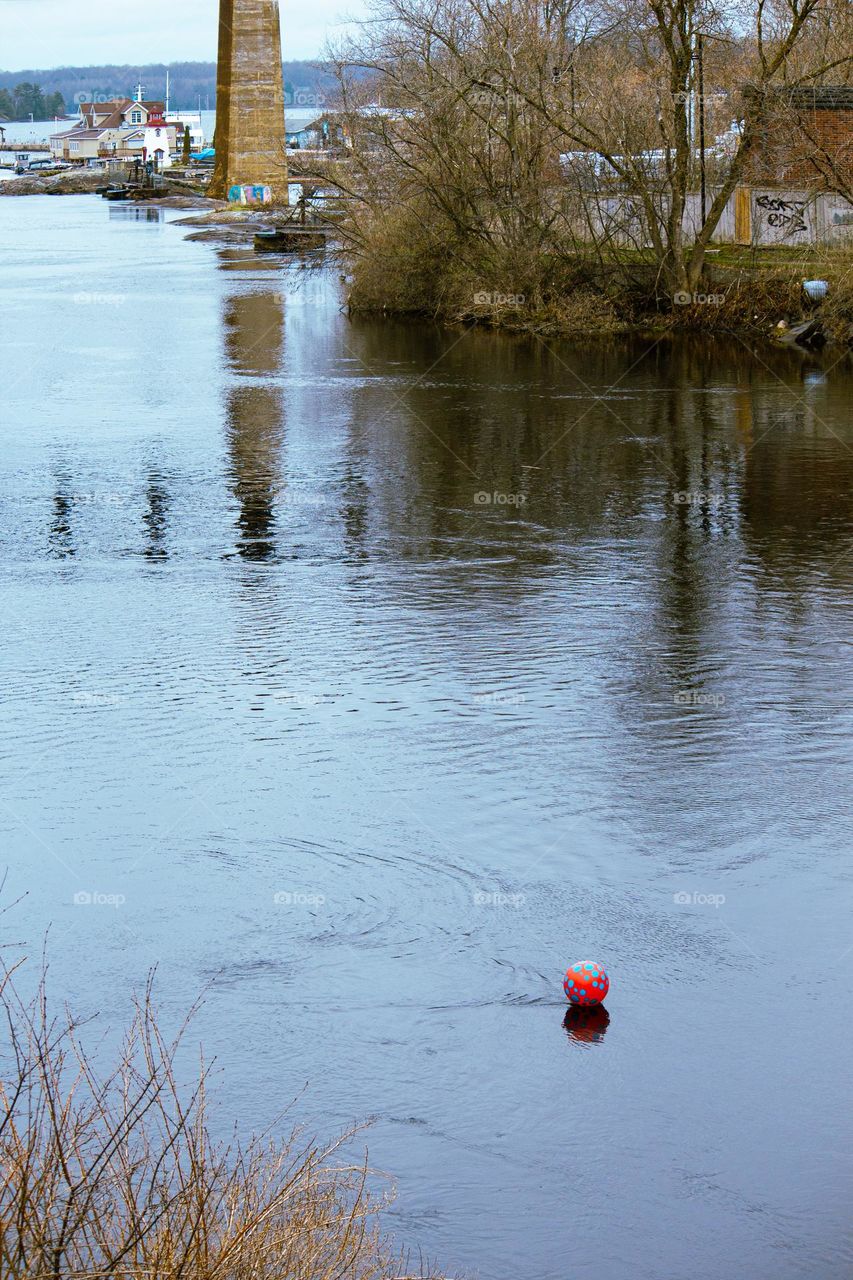 Pink beach ball floating down the lake with a marine town in the background.