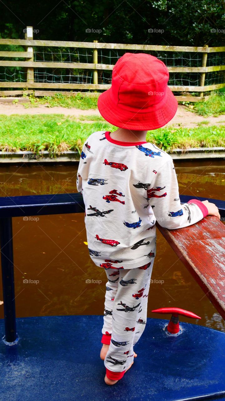 Kid stand on a boat in his pyjama red hat and barefoot 