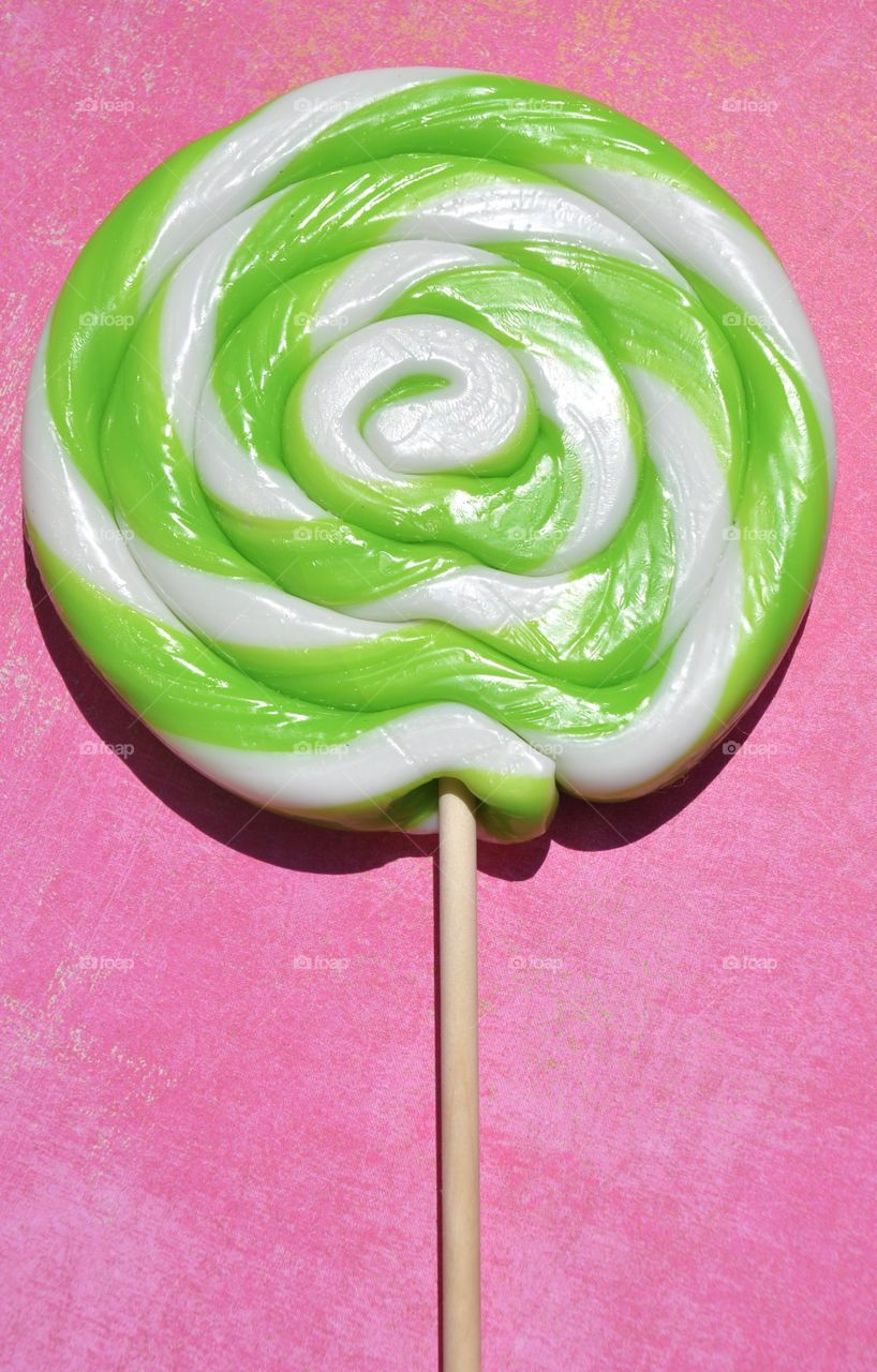 Green and white swirled lollipop against a bright pink background. 