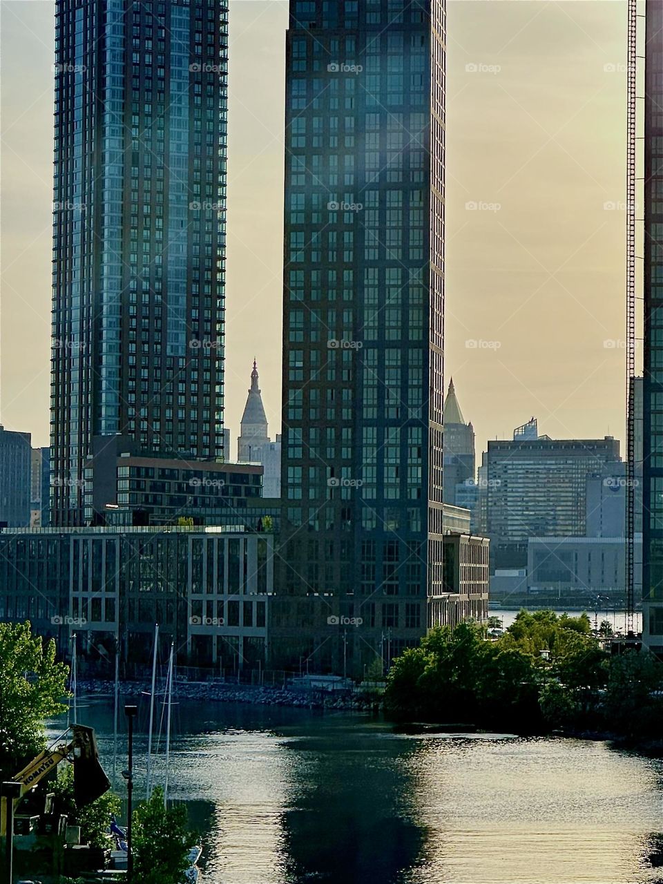 This is “Newtown Creek” seen from the “Pulaski Bridge” that connects LIC, Queens to “Greenpoint”, Brooklyn. Across the “East River” we see “Manhattan” zoomed in onto the “New York Life Building” with the golden roof. 2024. Hypnotic Productions
