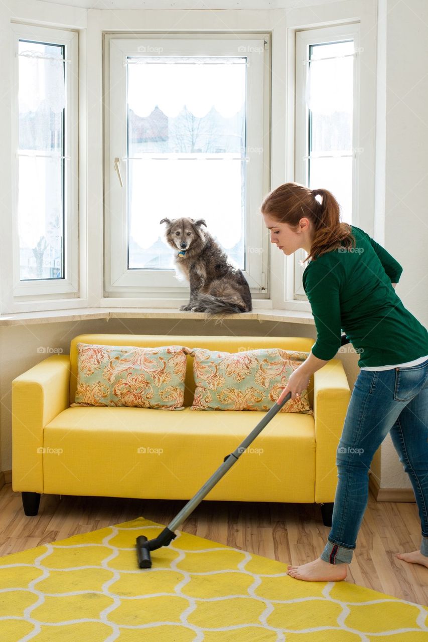 Woman vacuuming room with dog sitting near window