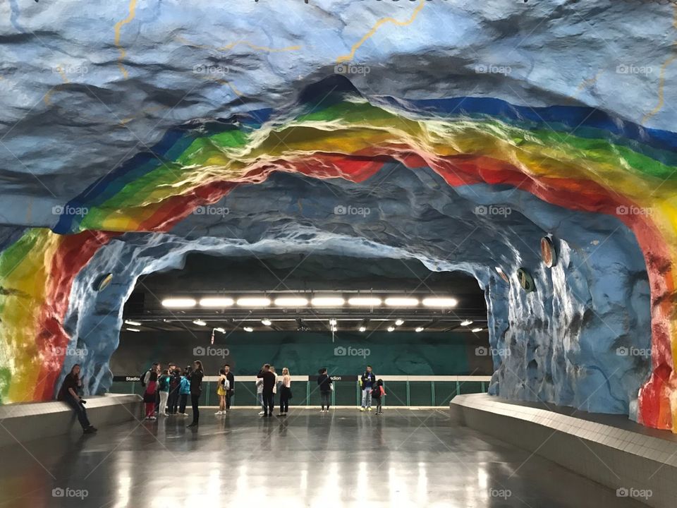 Metro stop “Stadion” in Stockholm, Sweden. People waiting for the metro to come under the lights and a large rainbow mural. 