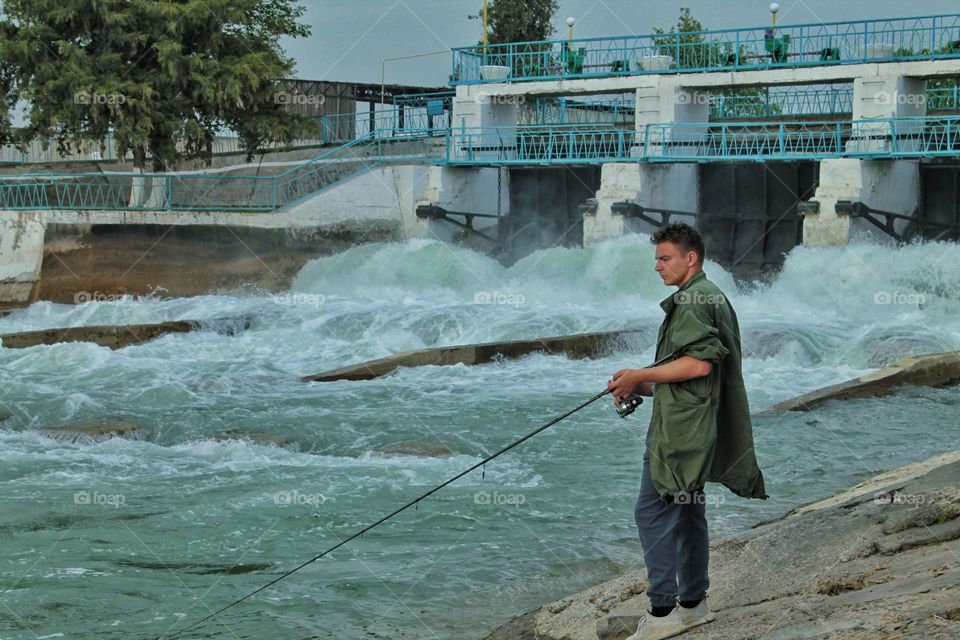 young fisherman catches fish on a spinning rod near the dam