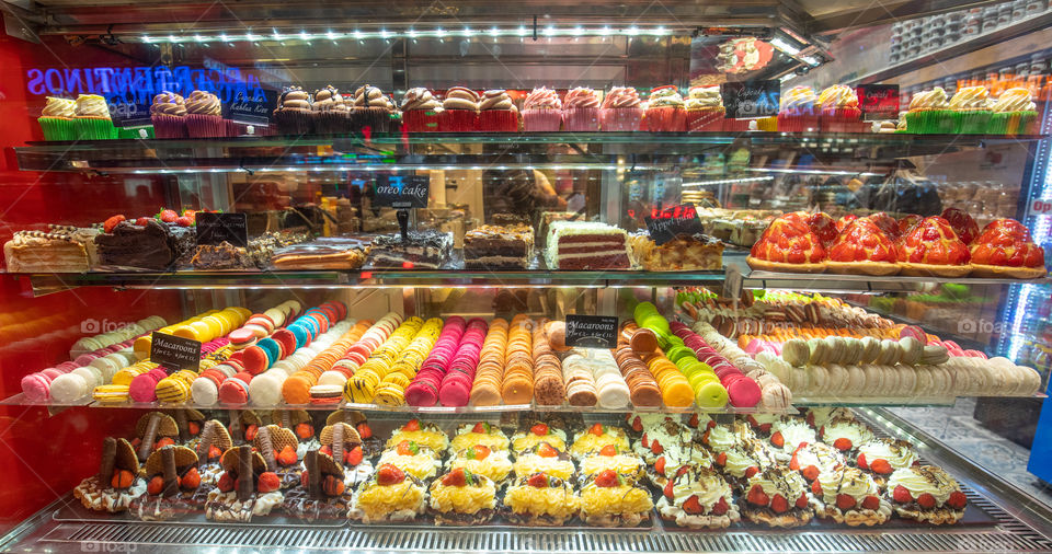 Colorful cup cakes, macarons, tarts, cakes, in a shop window. Candies, sweets and desserts at the store.