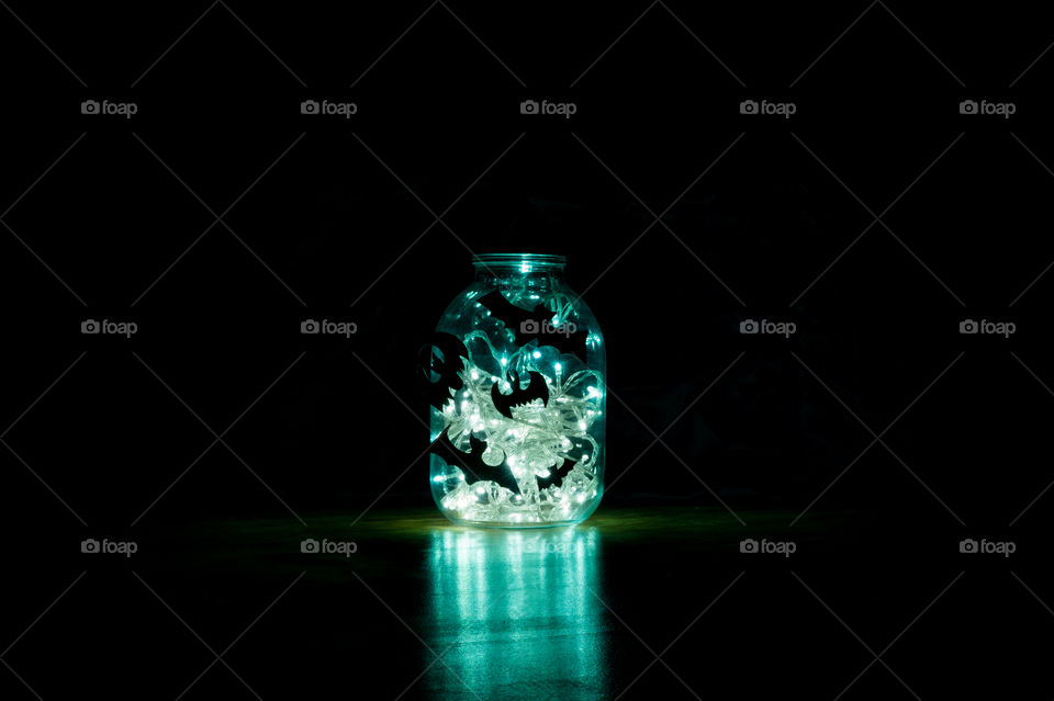 Halloween bats are glued to a glass jar with a garland glowing in it.