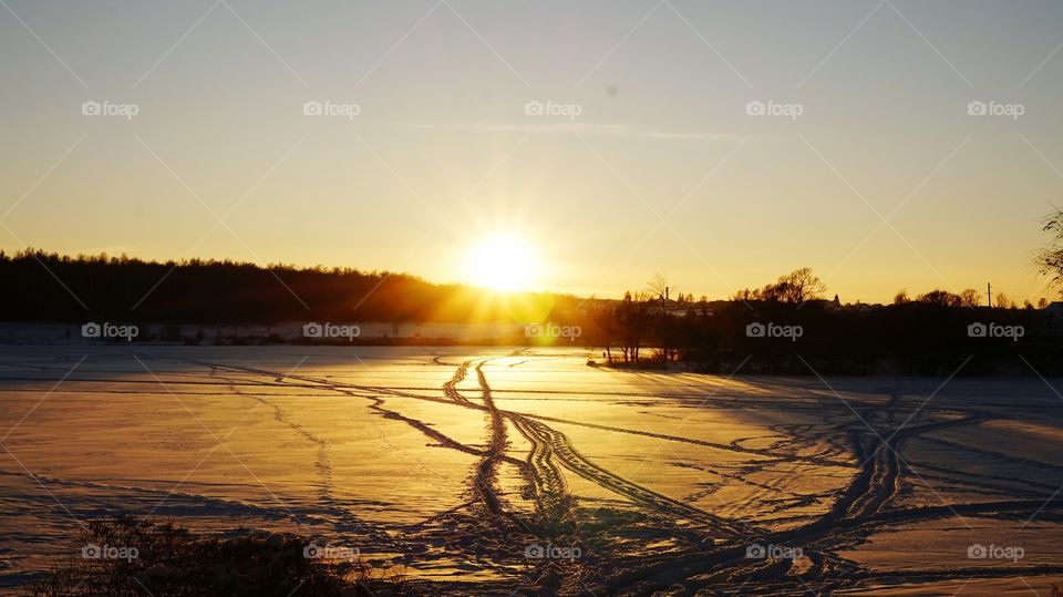View of silhouetted trees and snowy field during sunrise