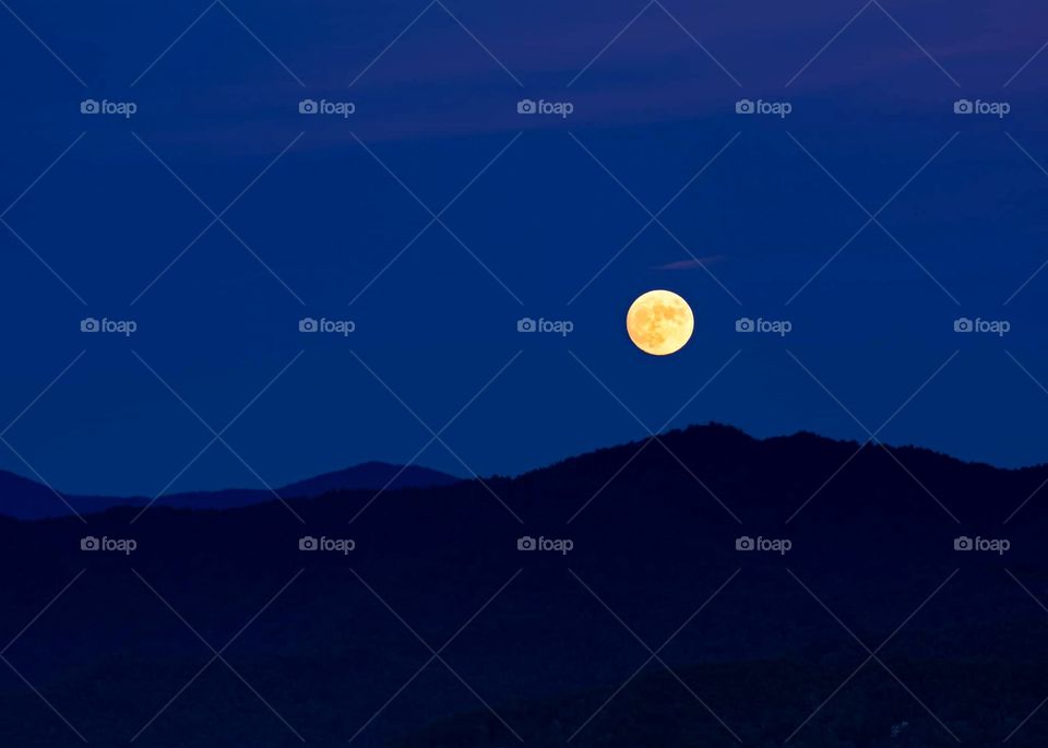 beautiful long range view of the autumn full moon over the smokey mountains of North Carolina USA during blue hour