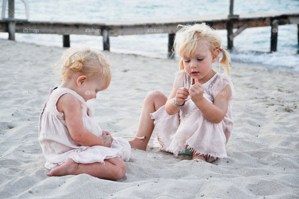 Cute sisters playing with sand at beach