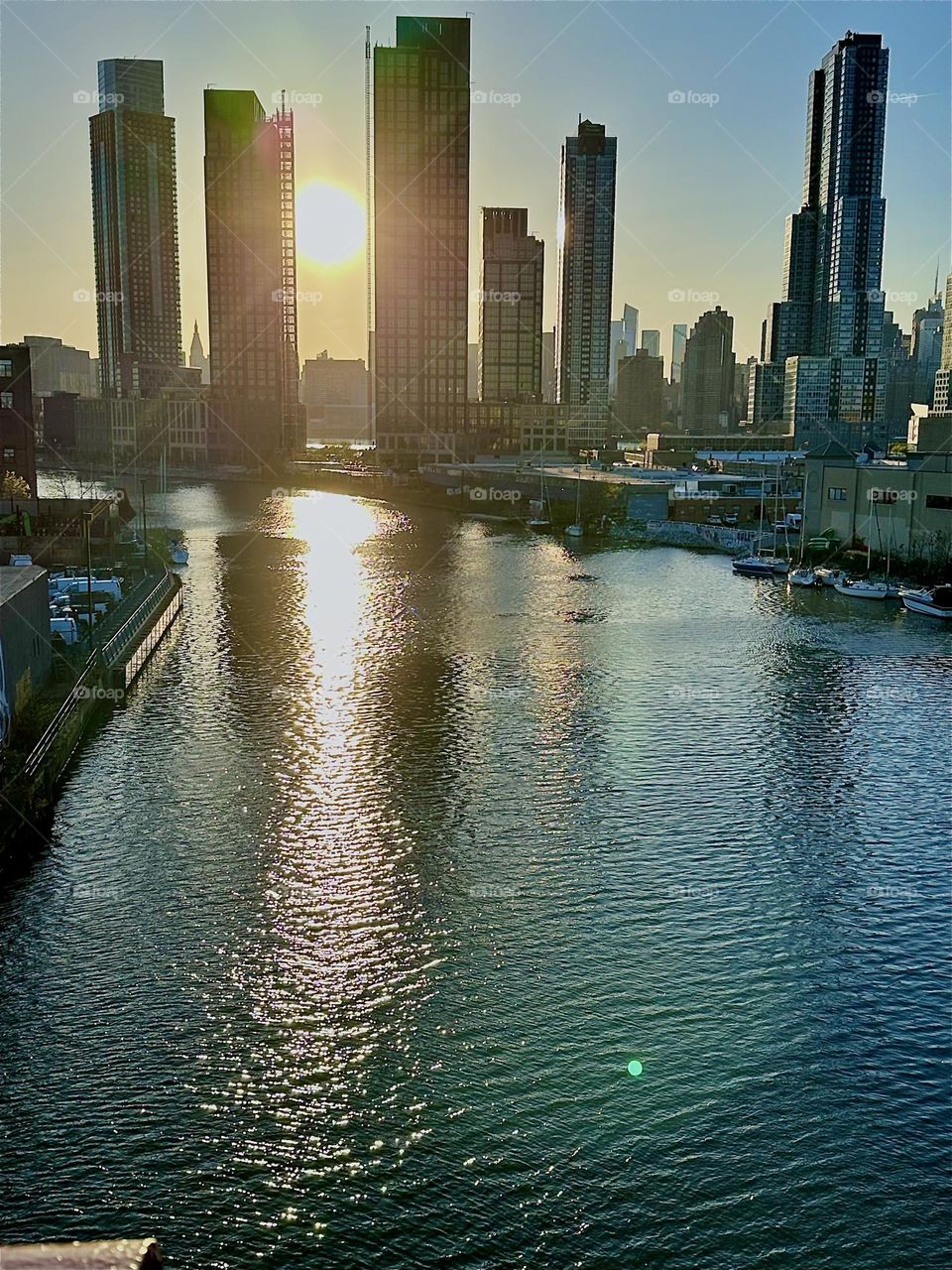 This is „Newtown Creek“ seen from the „Pulaski Bridge“ that connects „Greenpoint“, Bklyn to LIC. The „E River“ shimmers in intense tones of gold and silver at the golden hour of sunset. In the distance we see „Manhattan“. 2024. Hypnotic Productions
