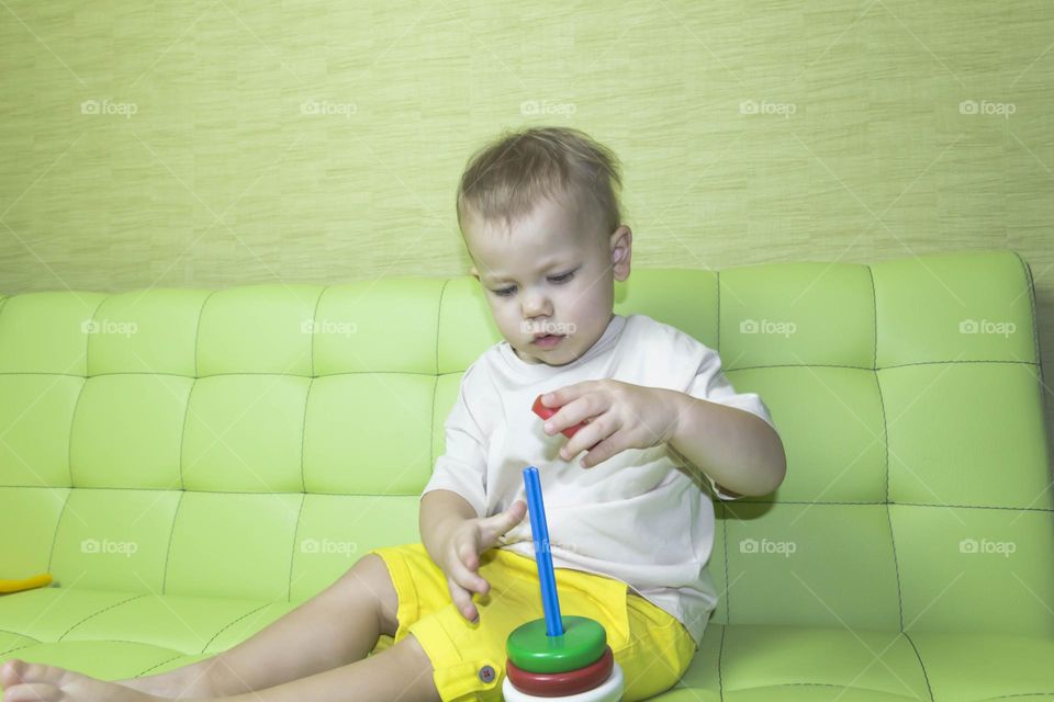 The child is having fun playing a bright pyramid educational toy, sitting on a green sofa.