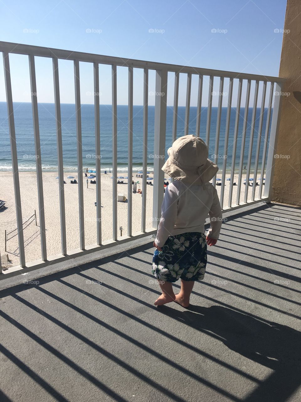 Toddler looking down at the beach from condo balcony 