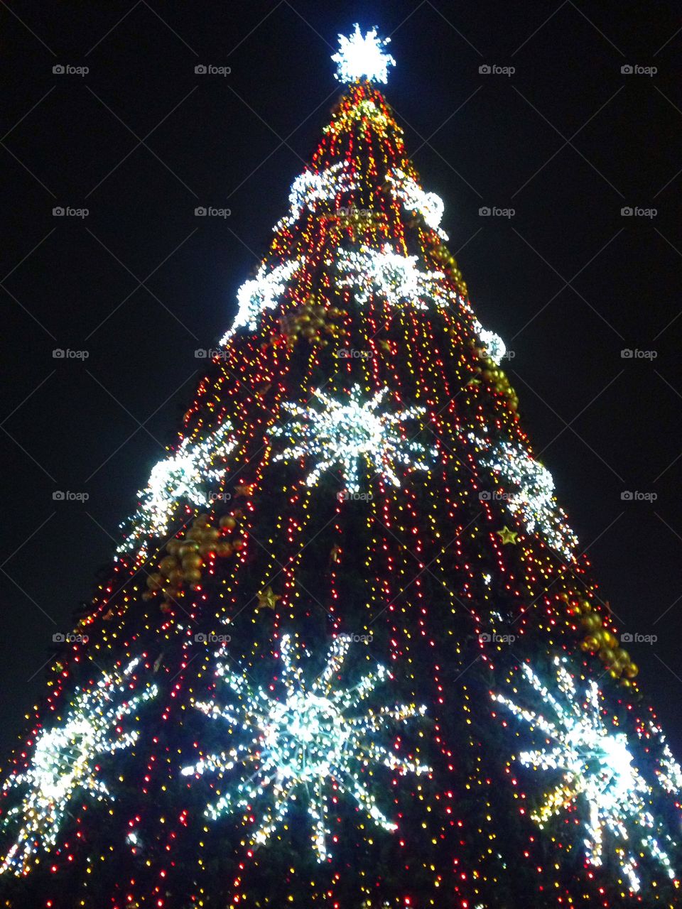 Bright colored illumination on artificial Christmas fir tree in the evening on black sky background in Moscow, Russia