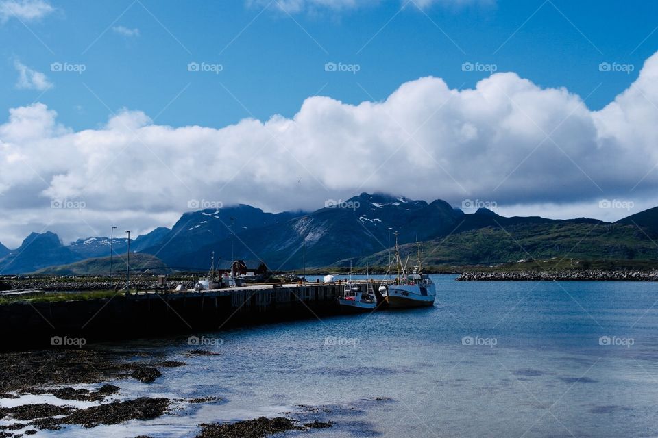 Arctic ocean on a sunny say with mountains behind and a harbour with some fishing boats 