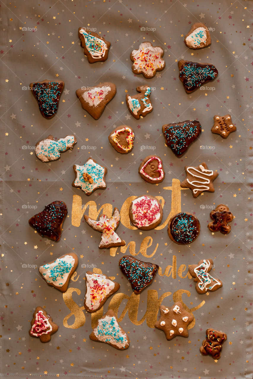 Christmas gingerbread cookies in many shapes decorated with colorful frosting, sprinkle, icing, chocolate coating, toppers, put on plain fabric