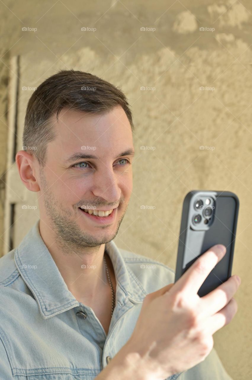 Portrait of a guy with dark hair who is smiling with phone in hand