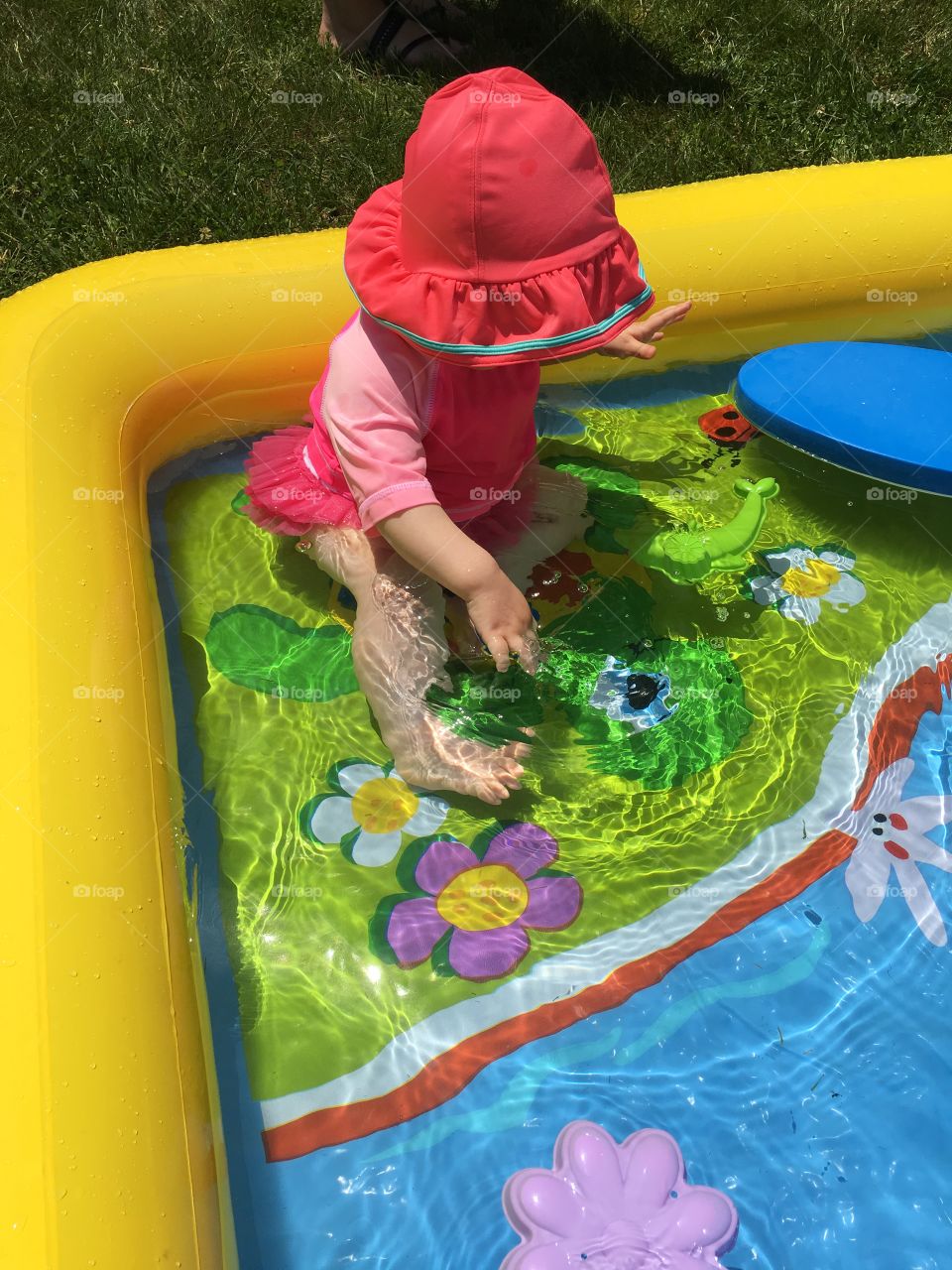 Baby girl splashing in a kiddie pool