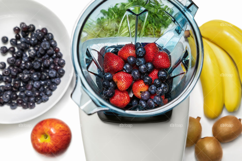 Series of shots. Photo 7. Blender in a top view, with ingredients for a smoothie. In this series we add strawberries and blueberries in an empty blender and bananas, kiwi, apple, sprouts on the table.