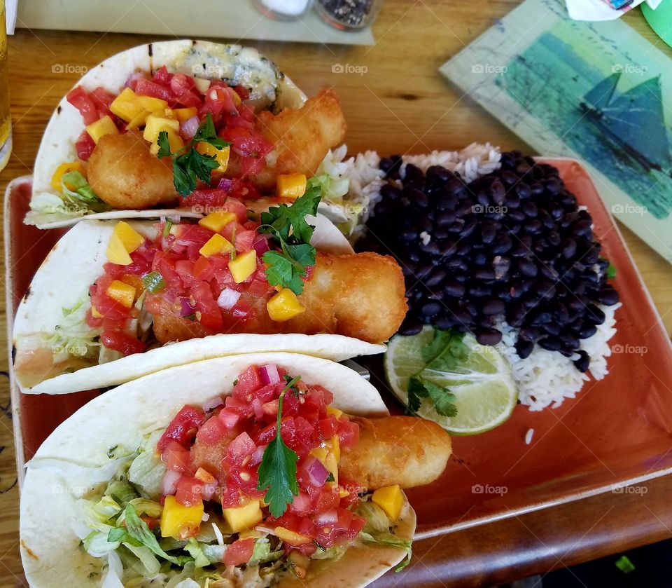 fish tacos on flour tortillas topped with mango salsa with a side of white rice and black beans.