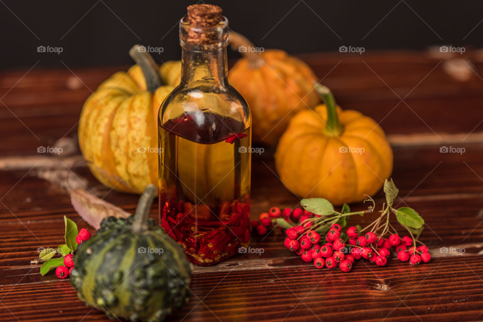 bottle of olive oil with chilli peppers on a rustic table, next to pumpkins, leaves and rowan