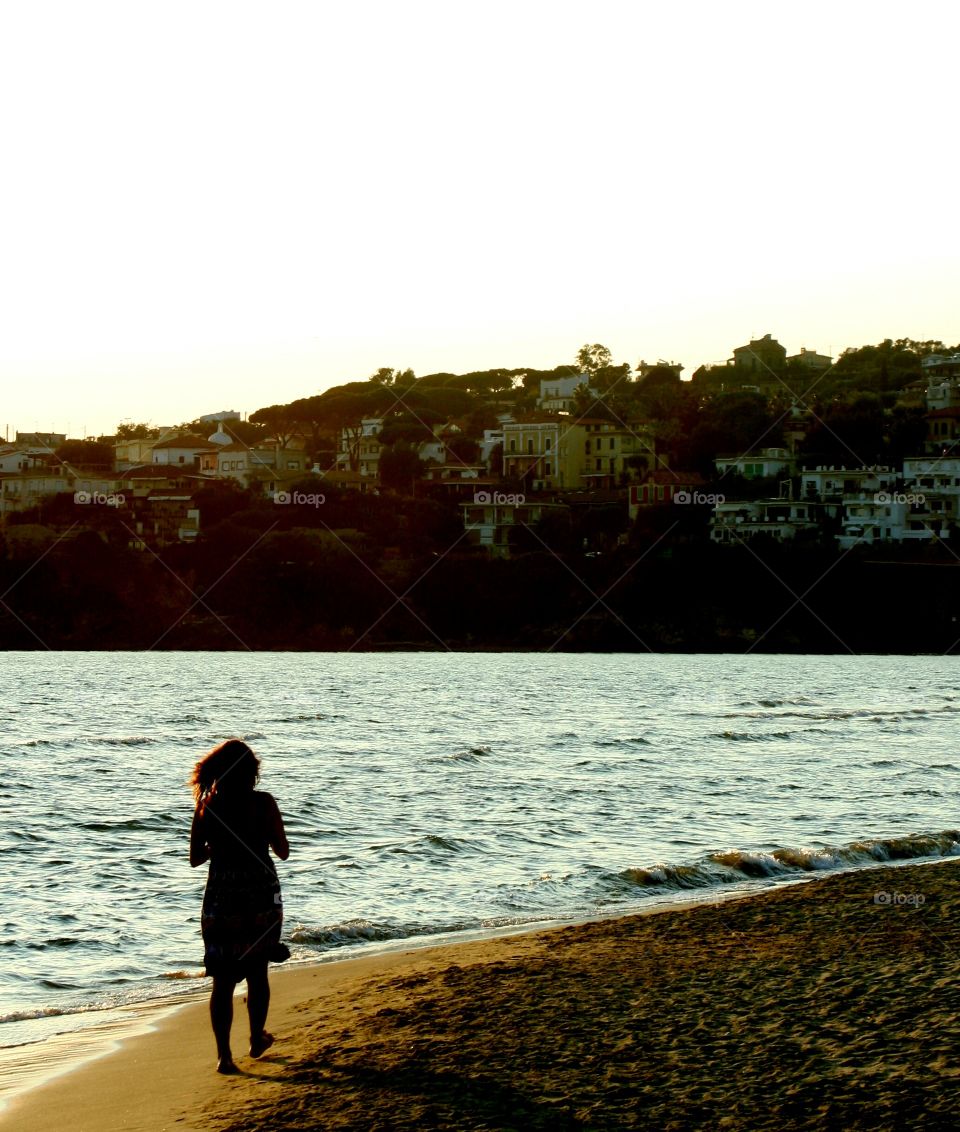 A woman checks her phone while taking a walk on beach in afternoon.
