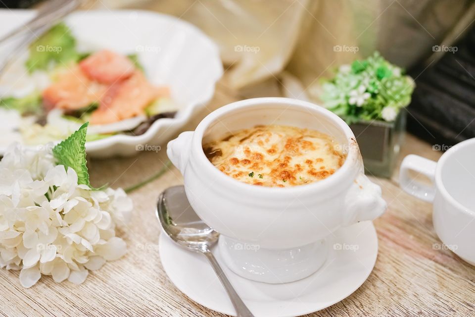 Onion soup with salmon salad on the background. Soft focus on the grilled cheese on top of onion soup.