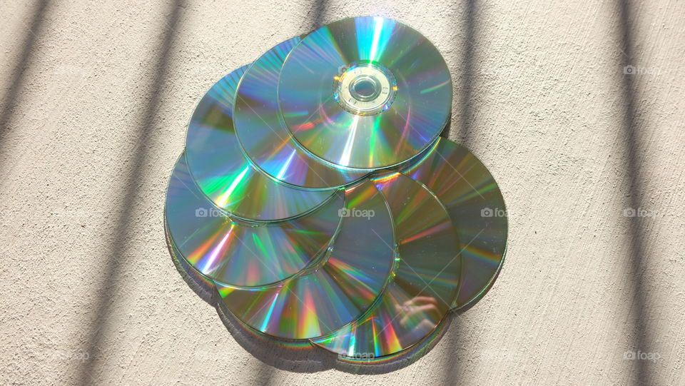 Boring grey cement background is a contrast to shiny CDs reflecting colorful lights.